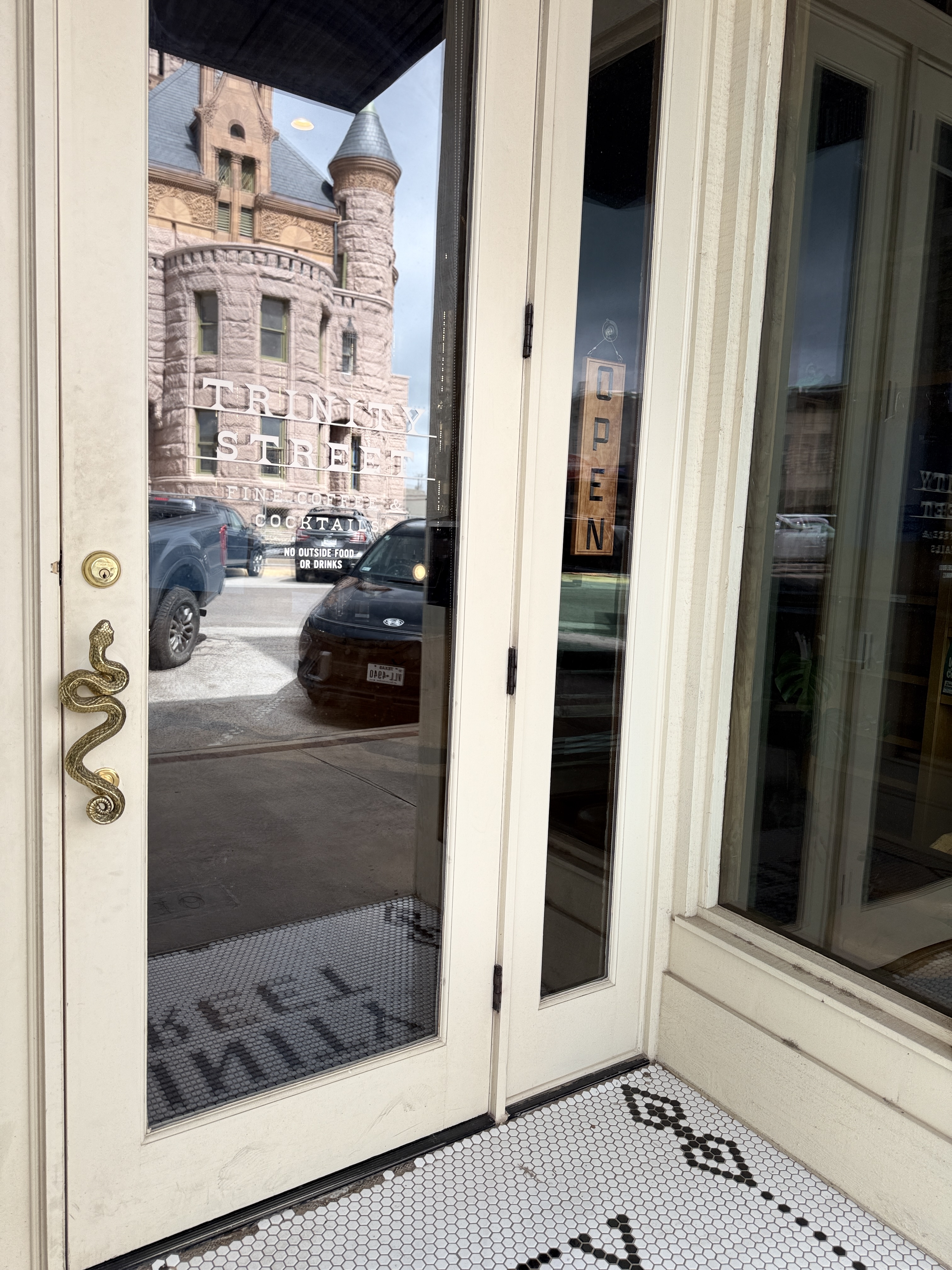 Intricate snake door handle on Trinity Street Coffee’s front door, with the reflection of the courthouse.